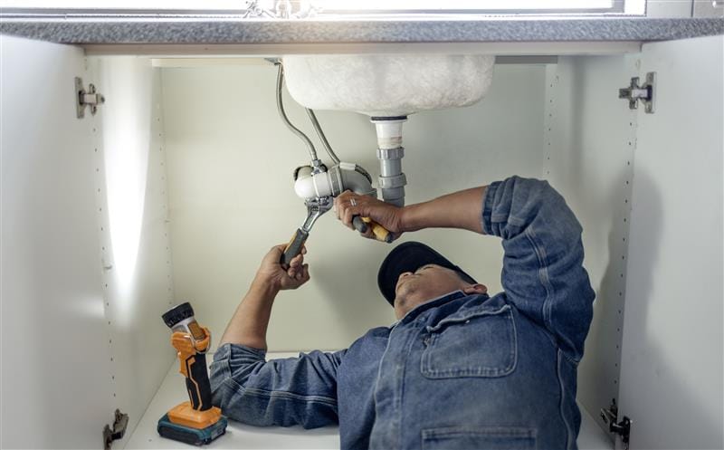 Plumber repairing pipes beneath a bathroom sink in Bethlehem