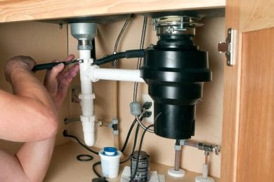 Plumber repairing a garbage disposal beneath a kitchen sink in Bethlehem