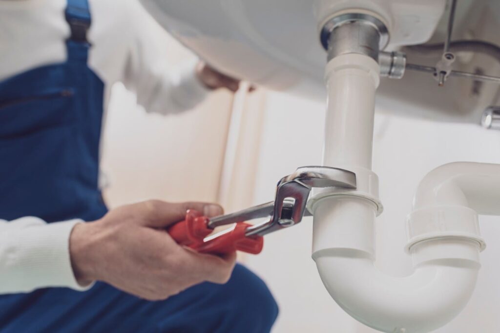 Plumber repairing a white drain pipe beneath a sink in Bethlehem